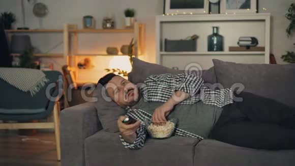 睡觉的男人看电视独自躺在沙发上吃爆米花视频的预览图
