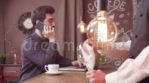 在酒吧柜台工作的时候男人用智能手机说话视频的预览图