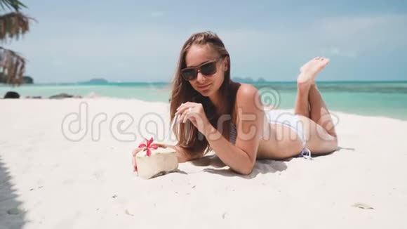 女人躺在沙滩上喝着椰子直视镜头视频的预览图