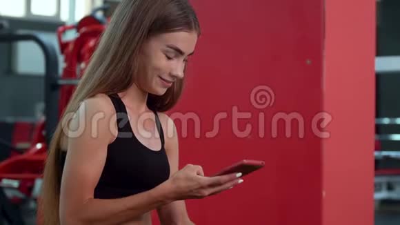 经过强化训练后美丽的女孩微笑着使用智能手机在长凳上休息视频的预览图