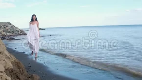 美丽的女孩光着脚在沙滩上散步微笑和旋转视频的预览图