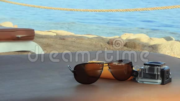 在阳光明媚的夏日在海边的一张桌子上放着太阳镜和一台用于水下拍摄的相机动作相机视频的预览图