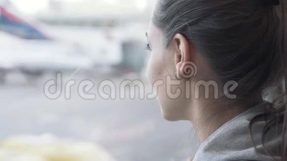 在飞机背景下向窗外眺望机场的美丽女孩的特写肖像视频的预览图