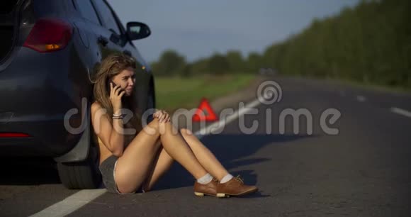 一个年轻的女人看着电话里的东西一辆破车在路上的车架上紧急视频的预览图