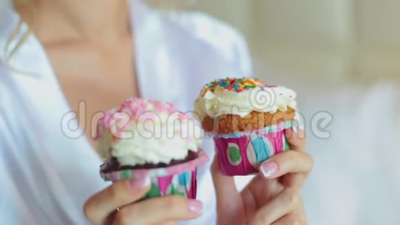 一个穿丝绸长袍的年轻女孩拿着纸杯蛋糕白色奶油和鲜艳的五彩洒视频的预览图
