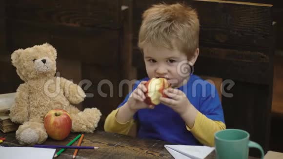 学校休息饥饿的孩子在教室里吃苹果桌上的小男孩在黑板前吃苹果小学生视频的预览图