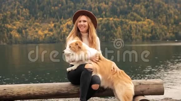 有趣的年轻女人带着狗边界牧羊犬在湖边遇见了女朋友在山脉的背景上视频的预览图