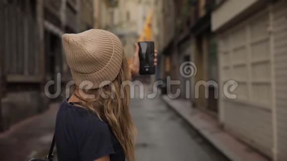 一位年轻时尚美丽的年轻千禧一代女士在一个欧洲老城区的街道上拍摄智能手机摄像头视频的预览图