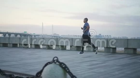 在夏季一个年轻的黑人非裔美国人迷人的健康男子在人行道上奔跑的近景视频的预览图