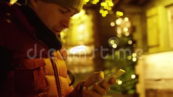 穿着红色夹克的英俊年轻人在晚上使用智能手机来抵御圣诞节的光照红色摄像机拍摄视频的预览图