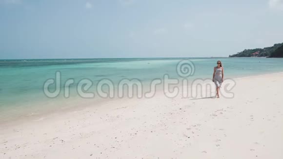 穿裙子戴太阳镜的女人在海滩上散步视频的预览图