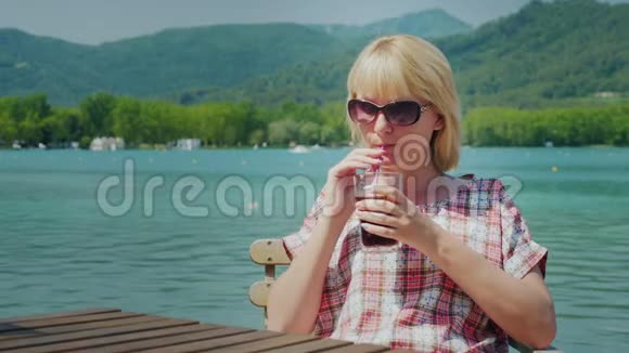 年轻的旅游妇女在西班牙湖边和山上的一个美丽的地方放松从杯子里喝可乐视频的预览图