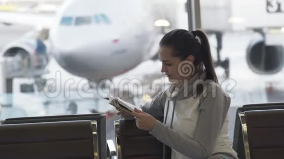 漂亮的女孩坐在机场休息室在窗外的飞机背景上看书视频的预览图