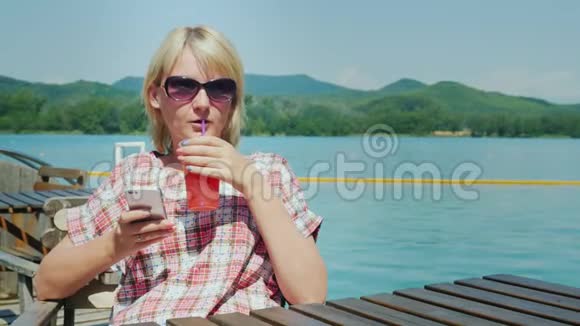 女人在咖啡馆的一个夏天休息它用电话背景中湖光山色度假村视频的预览图