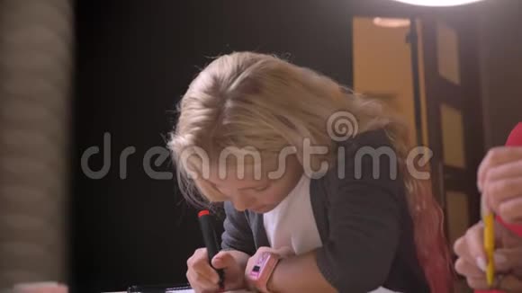 年轻漂亮的金发女孩在父母面前做作业的特写镜头视频的预览图