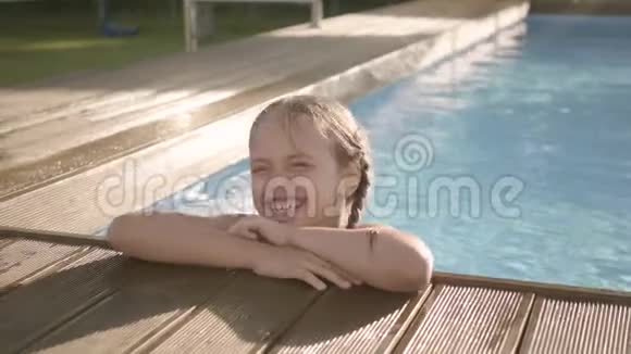 可爱的滑稽女孩扎着辫子笑拇指向上看着游泳池外抓住边缘普雷特儿童视频的预览图