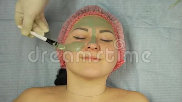 戴手套的美容师用一个治疗用的黏土面具罩在女人脸上视频的预览图