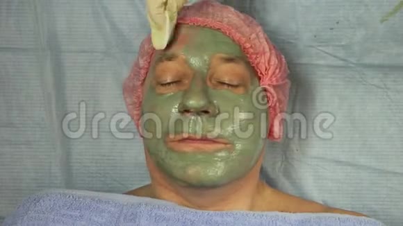 戴手套的美容师用一个治疗用的黏土面具一个男人的脸上用刷子视频的预览图
