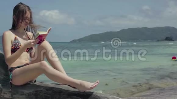 塞舌尔普拉斯林岛这位年轻貌美的女士坐在树干上看书在水上看书视频的预览图