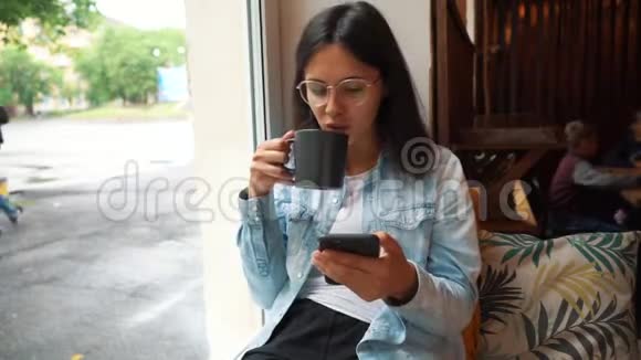 坐在咖啡店里的年轻女人女孩浏览互联网聊天博客女人拿着电话看着他视频的预览图