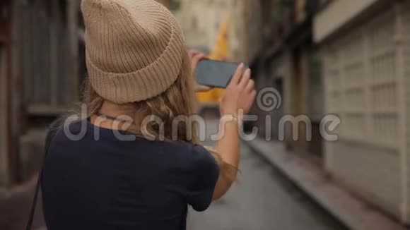 一位年轻时尚美丽的年轻千禧一代女士在一个欧洲老城区的街道上拍摄智能手机摄像头视频的预览图