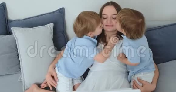 妈妈坐在沙发上拿着笔记本电脑两个男孩的孩子唱歌亲吻他们的母亲家庭幸福充满爱心视频的预览图