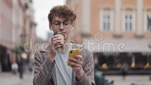 戴眼镜戴耳机的年轻嬉皮士使用社交网络中的智能手机打字信息喝咖啡视频的预览图