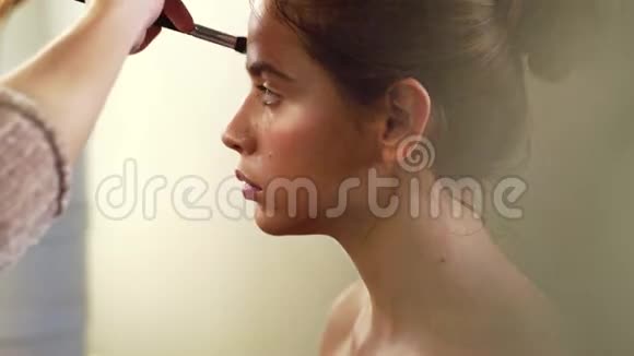 化妆的过程化妆师在模特脸上用刷子工作美容院年轻女子画像视频的预览图