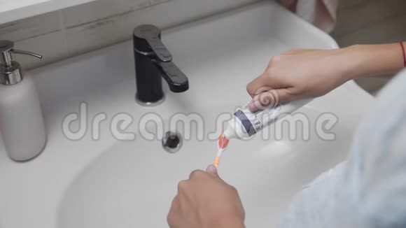年轻女子在浴室用牙刷刷牙近距离用手在刷子上挤压意大利面视频的预览图