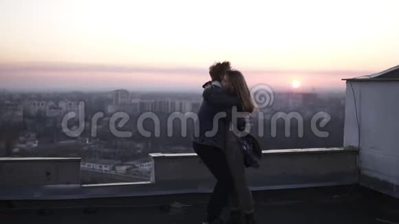 红头发的家伙在屋顶上旋转他的女朋友背景是城市景观和日落地平线一起度过快乐时光视频的预览图