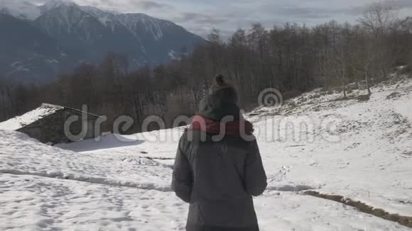一个女孩在山间小屋附近的雪地上行走的追踪镜头视频的预览图