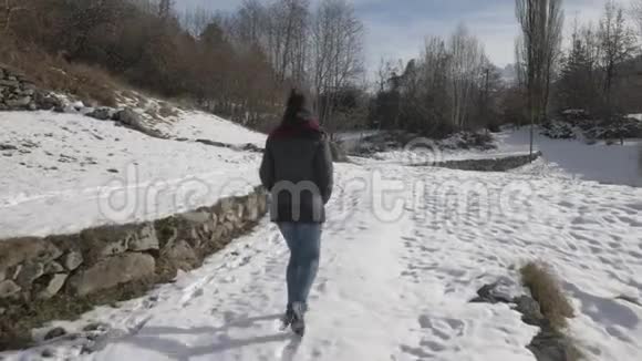 女孩走在雪地里的小路上稳定的跟踪镜头视频的预览图