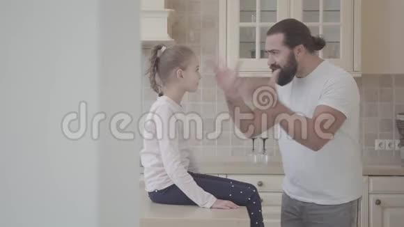 长胡子的男人有感情地给他的小女儿讲故事在厨房里积极地做手势女孩坐在上面视频的预览图
