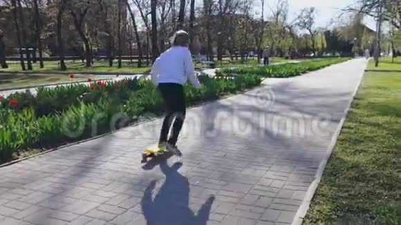 一个小女孩在阳光下骑着黄色的滑板在公园的中央视频的预览图