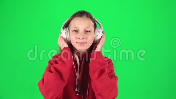 青少年女孩听音乐在绿色背景上戴着白色的大耳机移动慢动作视频的预览图