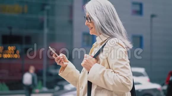 中年亚洲妇女站在街上用智能手机打字视频的预览图