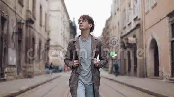 年轻的千禧一代戴着格子外套戴着带袋走路的耳机的牛仔裤环顾旧城视频的预览图