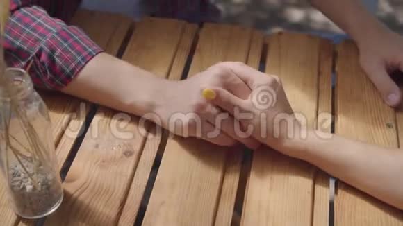 坐在桌旁的未被认出的年轻人和女孩的特写双手牵手男女约会视频的预览图