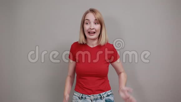 穿着红色衬衫的漂亮年轻女子看着灰色墙壁上的摄像机视频的预览图