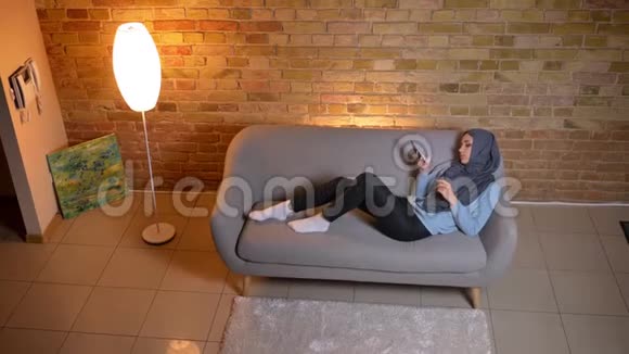 在室内沙发上放松的年轻迷人的穆斯林女性手机短信特写镜头视频的预览图