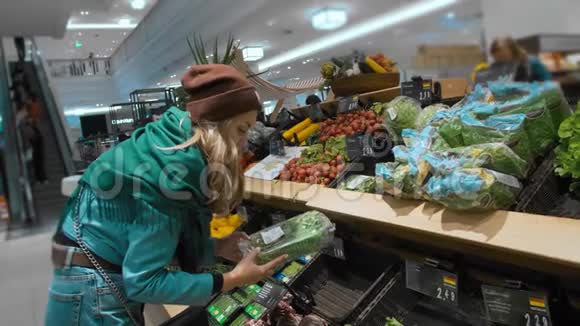 美丽的白种人女孩穿着蓝色夹克和绿色围巾选择并购买绿色蔬菜和健康产品视频的预览图