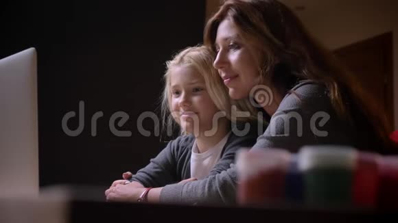 一位年轻的白种人母亲和一个美丽的小女儿一起看一幅漫画拥抱在一起拍摄特写镜头视频的预览图