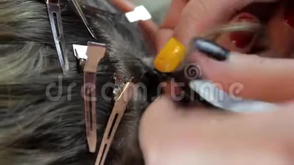 在理发师的特写镜头中有着彩色指甲的女性手编织出头发的辫子视频的预览图