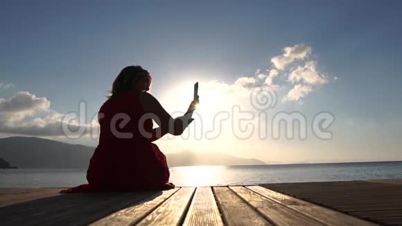 一个女人坐在海边慢镜头地拍着日出时的景色视频的预览图