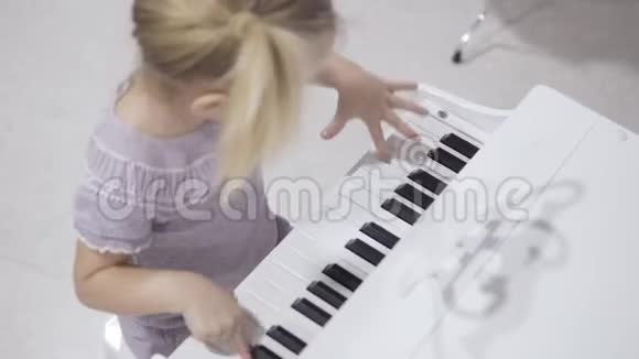 一个可爱的小女孩坐在时尚的孩子们钢琴和演奏音乐视频的预览图