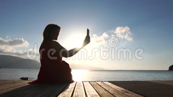 一个女人坐在海边在日出时拍照动作缓慢视频的预览图