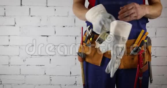 施工工人带着工具带站在白色砖墙背景上视频的预览图