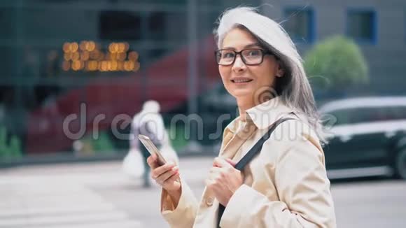 中年亚洲妇女站在街上用智能手机打字视频的预览图