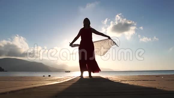 日出时一位戴着围巾的成年女子慢动作地站在海滩上视频的预览图