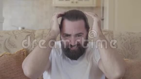 一个留着胡子的人坐在沙发上因为头痛得要命视频的预览图